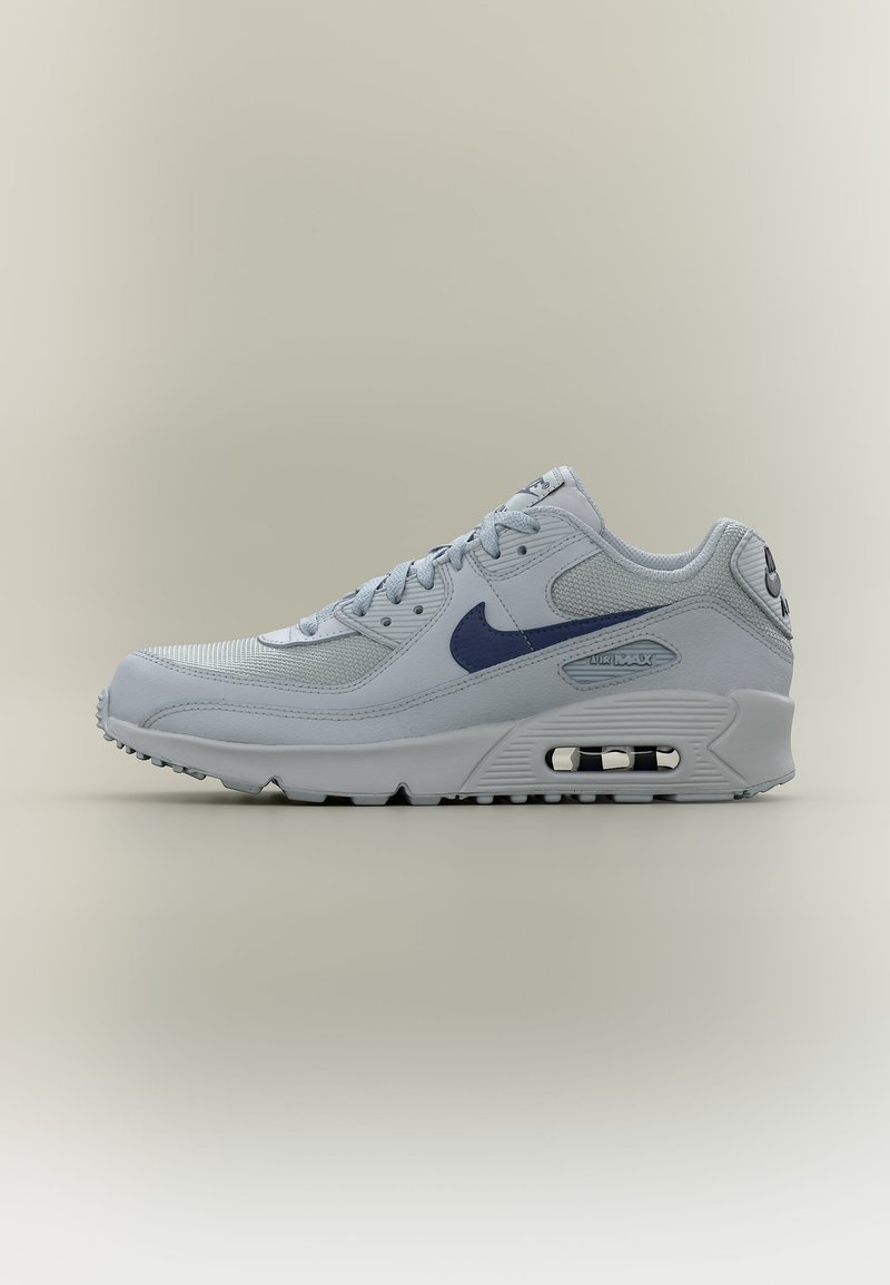 Šviesiai pilkasis Nike Air Max sportbačius su tamsiai mėlynu logotipu, akių ir odos viršumi, matoma oro pagalvėlė pado viduje, ant neutralaus fono.