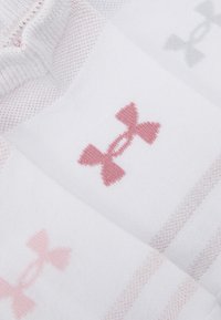 Hvite sokker med rosa og grå Under Armour-logoer. Stoffet er mykt med en ribbet tekstur og et subtilt stripet mønster.