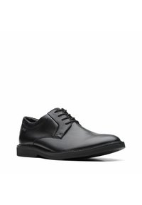Zapato de vestir de cuero negro con un acabado suave, punta redonda, diseño de cordones y una suela plana de goma. Presenta un detalle de costura mínima.