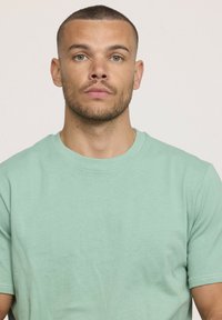 T-shirt en coton vert menthe avec un col rond classique et des manches courtes, présentant une texture lisse et un subtil détail de couture.