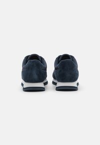 Des chaussures de sport bleu marine avec une finition en daim lisse et texturé, une semelle intermédiaire blanche contrastante et un talon rembourré pour le confort.