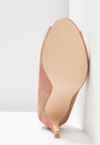 Soleansicht eines spitz zulaufenden Kitten-Heels mit einem pink glitzernden Obermaterial und hellbeigem, glattem Outsole.