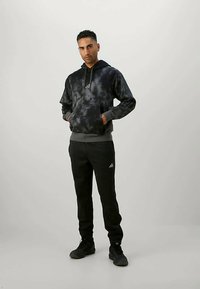 Μαύρο hoodie με σχέδιο tie-dye και κορδόνι, συνδυασμένο με μαύρες φόρμες joggers που διαθέτουν το λογότυπο της Adidas. Και τα δύο ρούχα είναι κατασκευασμένα από μαλακό, άνετο ύφασμα.