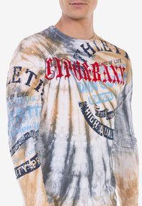 Langärmliges Batik-Shirt in Beige und Grau mit blauen und roten grafischen Drucken; verfügt über verschiedene Texte und runde Akzente im gesamten Design.