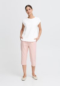 Vit bomull t-shirt med korta ärmar, kombinerat med ljusrosa capribyxor. Outfiten inkluderar mönstrade slip-on skor.