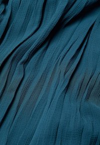 Tissu texturé bleu sarcelle avec des plis verticaux, présentant une apparence douce et légère ainsi qu'une surface légèrement froissée.