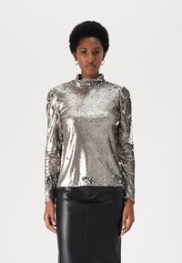 Silberner Pailletten-Top mit langen Ärmeln und hohem Kragen; glatte Textur mit glänzendem Finish; kombiniert mit einem schwarzen Lederrock.