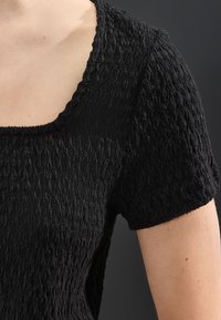 Mustast tekstuuriga topp ruudukujulise kaeluse ja lühikeste varrukatega, valmistatud kortsus kangast, rõhutades selle ainulaadset pindmist detaili.