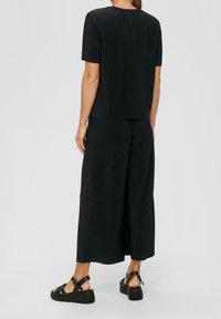 Top negro de canalé y pantalones de pierna ancha, con un ajuste relajado. Combinado con sandalias de plataforma negras. Diseño simple con detalles mínimos.