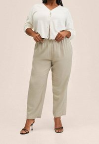 Lichtbeige losse broek met een elastische tailleband, gecombineerd met een witte knopencardigan en zwarte sandalen met bandjes.