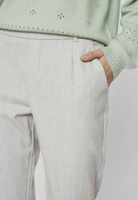 Pantalons en lin gris clair avec une coupe droite, dotés de poches latérales. Associé à un pull en tricot vert menthe avec des détails perforés.
