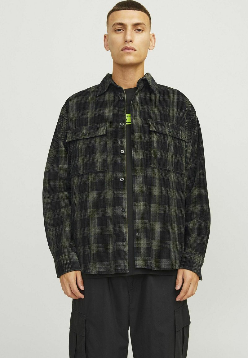 Zwarte en groene geruite overhemd met een losse pasvorm, voorzien van twee borstzakken en knoopsluiting, gelaagd over een zwart T-shirt.
