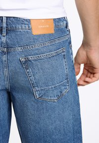 Blauwe denim jeans met een vervaagde afwerking, voorzien van een achterzak en een leren label in bruin met de tekst "JUNK de LUXE" nabij de tailleband.