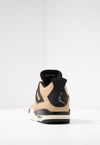 Baskets Air Jordan beige et noires vues de dos sur une surface blanche et un fond blanc.