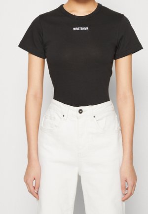 Sort t-shirt med korte ærmer lavet af bomuld, med rund hals og hvid tekst "WRSTBHVR" på brystet. Kombineret med hvide, højtaljede jeans.