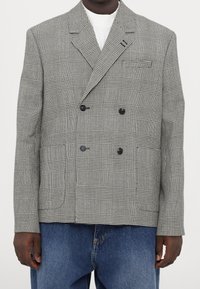 Dwurzędowa marynarka w czarno-białą kratę. Posiada wyraźny kołnierz, dwie przednie kieszenie i czarne guziki. Noszona na dżinsie.