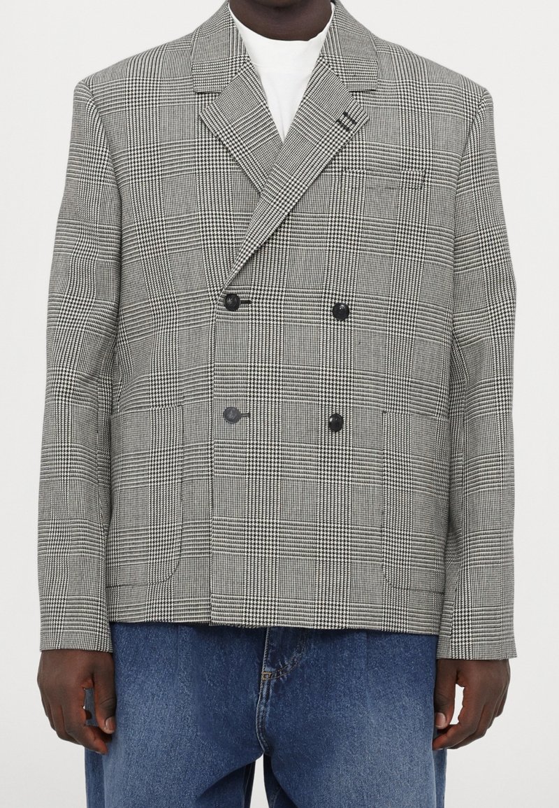 Dwurzędowa marynarka w czarno-białą kratę. Posiada wyraźny kołnierz, dwie przednie kieszenie i czarne guziki. Noszona na dżinsie.