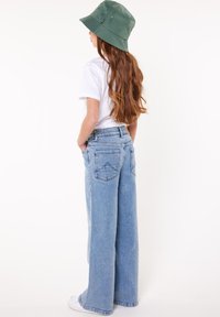 Jeans de mezclilla de corte ancho en azul claro con una cintura alta, bolsillos traseros y un acabado texturizado, combinados con una camiseta blanca y un sombrero tipo cubo verde.