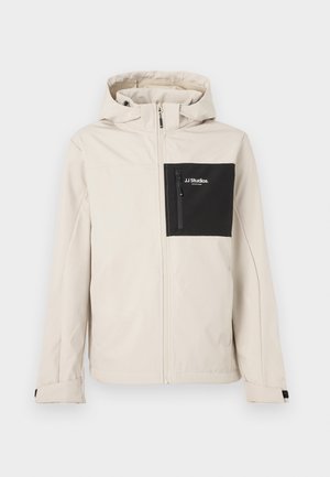 Veste beige à capuche avec fermeture éclair intégrale à l'avant, poche poitrine zippée noire étiquetée "JJ Studios" sur le côté gauche, poignets réglables.