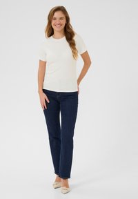 Witte ribbelde T-shirt met korte mouwen en een gekartelde halslijn, gecombineerd met donkerdenim jeans en beige ballerina's.