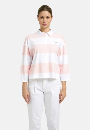 Woman wearing a pink and white horizontal striped long-sleeve polo with a small cocktail glass embroidery, paired with white pants.