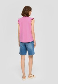 Różowa bluzka z krótkim rękawem z falbanami, w połączeniu z niebieskimi szortami dżinsowymi z postrzępionym dołem oraz beżowymi sandałami z klamrami.