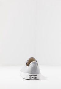 Szare płócienne sneakersy z okrągłym noskiem, białą gumową podeszwą i logo "CONVERSE ALL STAR" na pięcie. Gładka tekstura i niski profil.