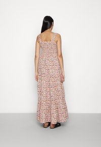 Robe longue fleurie avec un corsage smocké, des bretelles épaisses et une jupe à volants dans des tons rose, jaune et bleu. Tissu texturé avec des motifs vibrants.