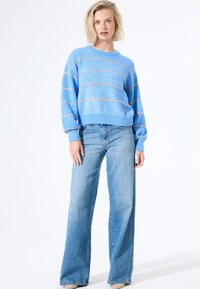 Helles blaugeplüschtes Sweatshirt mit horizontalen orangenen Streifen, gerippten Bündchen und Saum, kombiniert mit hoch taillierten hellblauen Jeans im lässigen Schnitt.