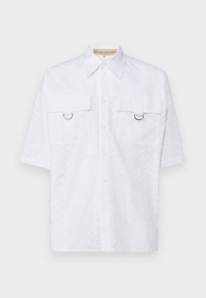 Camicetta bianca a maniche corte con dettagli in pizzo, due tasche frontali e opzioni di fissaggio in metallo argentato. Design con bottoni e colletto classico.