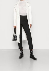 Vit lång kappa, mönstrad vit topp, svarta åtsittande byxor och svarta ankelstövlar. Tillbehören inkluderar en liten svart axelväska.