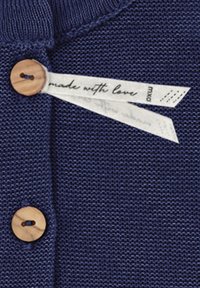 Marineblaue Strickware mit einem Holzknopf und einem weißen Etikett mit der Aufschrift "mit Liebe gemacht", das eine subtile Textur und ein weiches Gewebedesign aufweist.