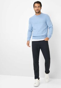 Lichtblauwe gebreide trui met een gestructureerd ontwerp, zwarte broek en witte sneakers. De trui heeft een ronde hals en ribgebreide manchetten.