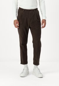 Brune kordfløyelsbukser med en teksturert overflate, med elastisk midje, legg og avsmalnende ben, kombinert med hvite joggesko.