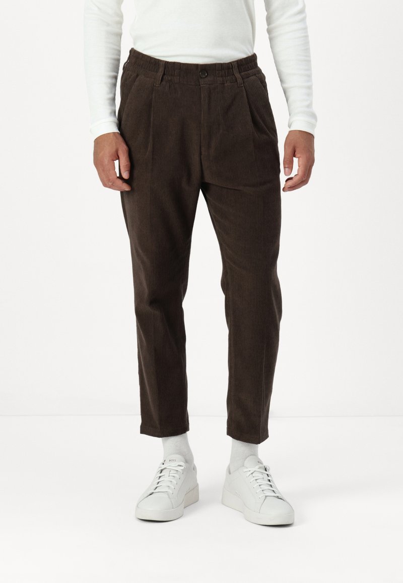 Brune kordfløyelsbukser med en teksturert overflate, med elastisk midje, legg og avsmalnende ben, kombinert med hvite joggesko.