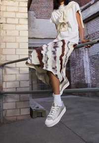 Bílé tričko s žebrovanými akcenty, splývavá sukně s červenými a fialovými proužky a stříbrné sneakers na platformě s bílými podrážkami.