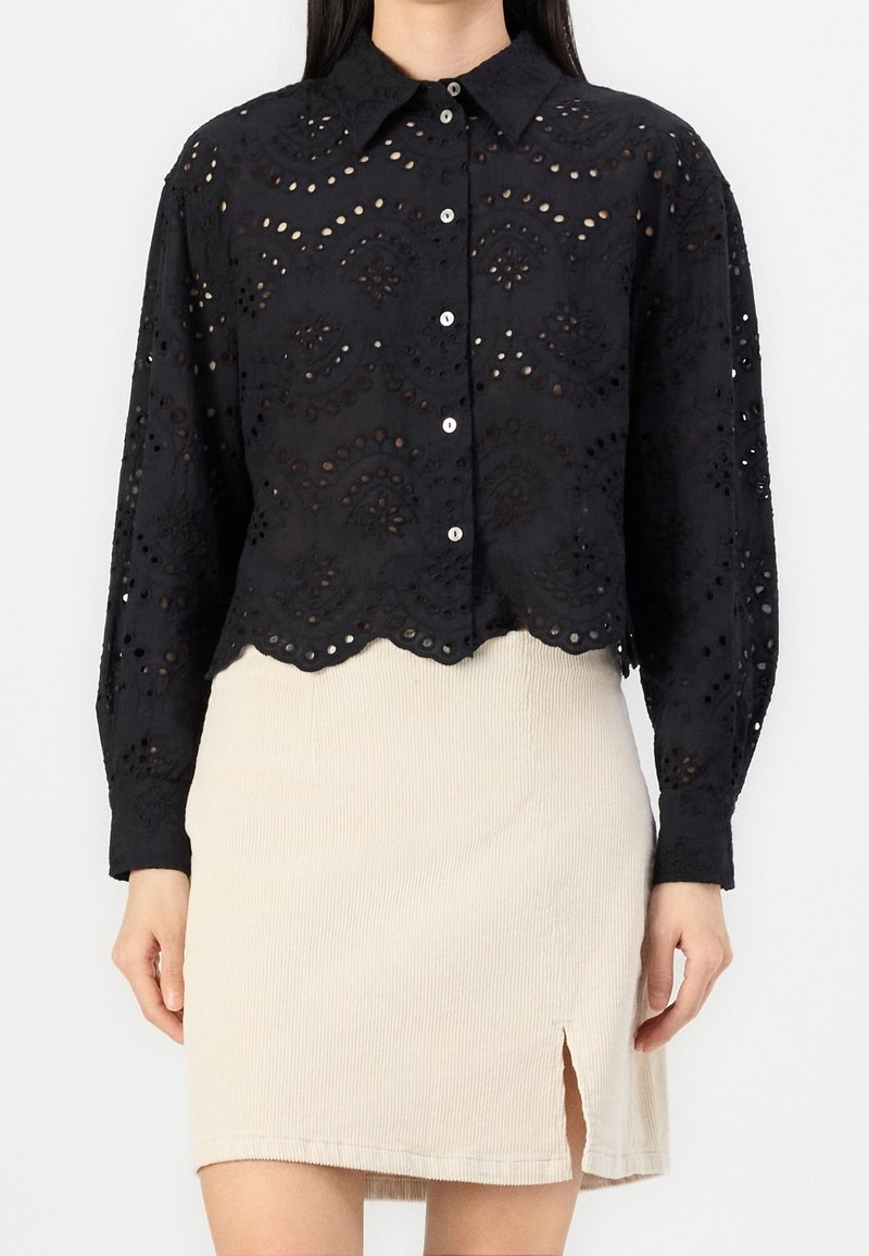 Black, long-sleeve, button-up shirt with eyelet embroidery and scalloped hem, featuring a structured collar and textured fabric.