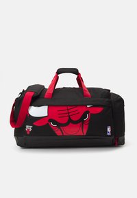 Schwarze Reisetasche mit roten Akzenten und einem großen, grafischen Chicago Bulls-Logo auf einer Seite. Verfügt über zwei Griffe und einen Schultergurt.