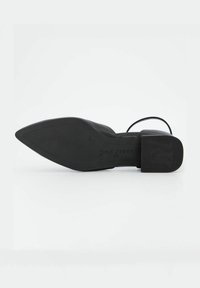 Chaussure à talons hauts noire avec un bout pointu et un dessus en cuir lisse. Caractérisée par un talon bloc avec une semelle texturée. Marque visible sur le talon.