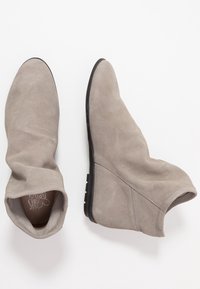Stivali alla caviglia in suede grigio con una forma affusolata, gambale flessibile e suola in gomma nera. Texture liscia con dettagli di cucitura minimi.
