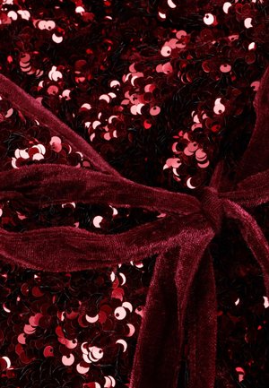 Bordeauxroter Stoff bedeckt mit glänzenden roten Pailletten und einem weichen Samtband. Die Textur wirkt glatt und reflektierend, was die visuelle Tiefe verstärkt.