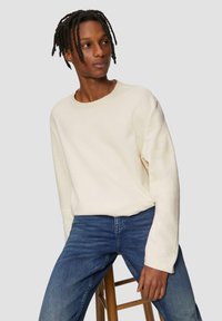 Cremefarbenes Sweatshirt mit langen Ärmeln aus Baumwollmischung, Rundhalsausschnitt, lockere Passform, kombiniert mit dunkelblauen Jeans. Einfaches Design.