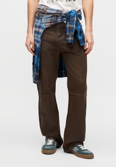 Κάπρι παντελόνια καφέ με φαρδιά γραμμή και ομαλή υφή, με ραφές στο γόνατο. Συνδυασμένα με μπλε πουκάμισο καρό δεμένο στη μέση και πράσινα αθλητικά παπούτσια.