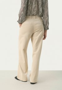 Beige corduroy levele-leg-housut, joissa on pystysuora ribbaus, sekä normaali vyötärö ja lantiotaskut. Suunniteltu rentoa istuvuutta varten.