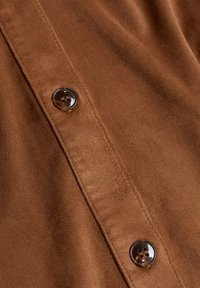 Gros plan d’un tissu marron avec deux boutons marron foncé à quatre trous cousus sur une patte cousue.