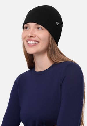 Gorra de punto negra con un ajuste ceñido, que presenta una pequeña etiqueta de logotipo. Se lleva con una camiseta de manga larga ajustada en color azul marino, de textura suave y diseño sin costuras.