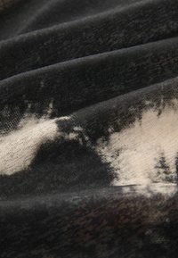 Tissu noir et beige avec une surface texturée, comportant un motif distinct en forme de nuages et des plis ondulés, présentant une apparence douce et mélangée.