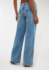 Jeans a gamba larga di colore blu chiaro in denim, con vita alta, tasche posteriori e orlo sfilacciato alla caviglia.