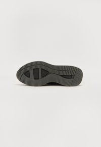Semelle d'une basket, avec un matériau en caoutchouc noir texturé, un motif de semelle pour l'adhérence et un design moulé pour le soutien.