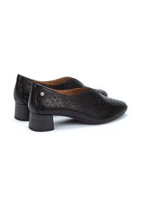 Chaussures en cuir noir avec un motif floral perforé, bout arrondi et un petit talon carré. Doublure intérieure marron et détails matériels minimaux.